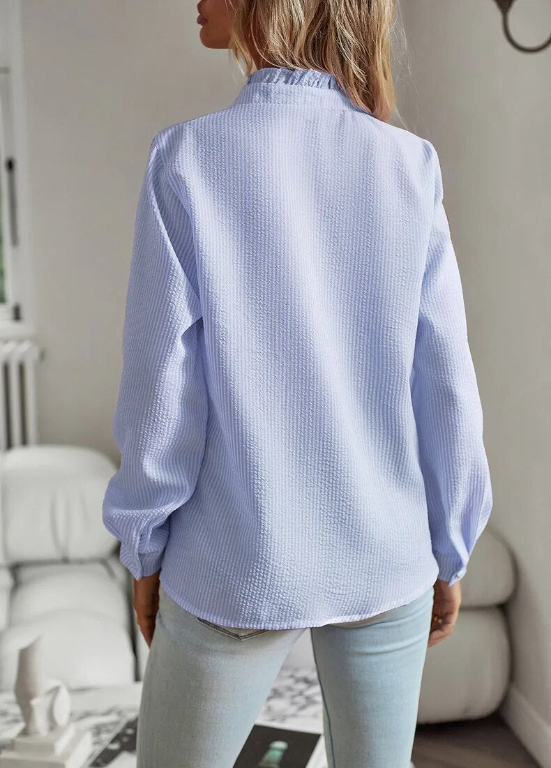 Donna con camicia a maniche lunghe azzurra, tessuto a trama leggera, in un ambiente interno moderno. Moda femminile, abbigliamento casual elegante.