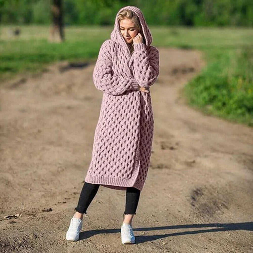 Donna con cappotto lungo a maglia rosa, cappuccio, su strada sterrata. Moda autunnale, abbigliamento casual, stile confortevole.