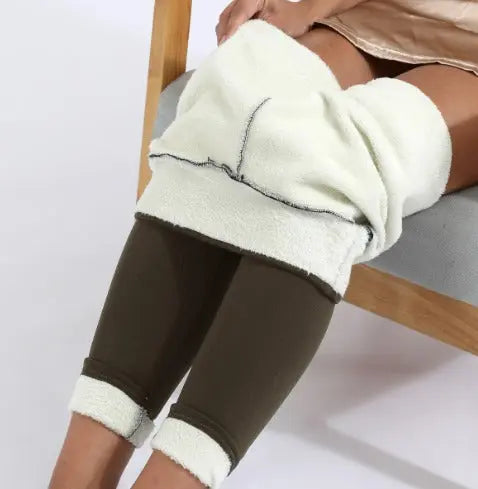 Donna seduta con coperta in pile bianca sulle gambe, indossa leggings marroni. Comfort, relax, abbigliamento casual, arredamento moderno.
