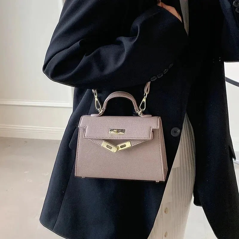 Borsa a mano elegante in pelle rosa tenue, indossata con giacca nera. Design classico, chiusura metallica dorata. Accessorio moda donna.