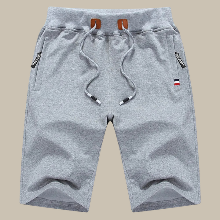Pantaloncini sportivi grigi da uomo in cotone, con coulisse e tasche laterali con zip. Design casual, ideale per palestra e tempo libero.