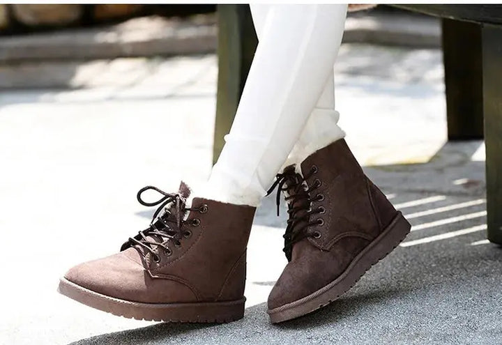Scarponcini invernali marroni da donna, con lacci, indossati con pantaloni bianchi. Calzature moda casual, comode e calde per la stagione fredda.