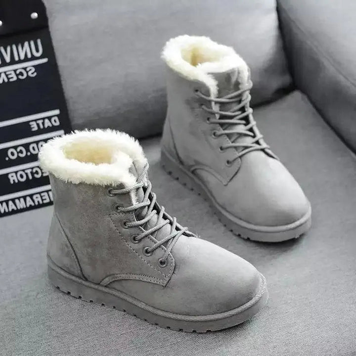 Stivali invernali grigi da donna con fodera in pelliccia sintetica, su divano grigio. Scarpe calde, moda inverno, calzature casual eleganti.