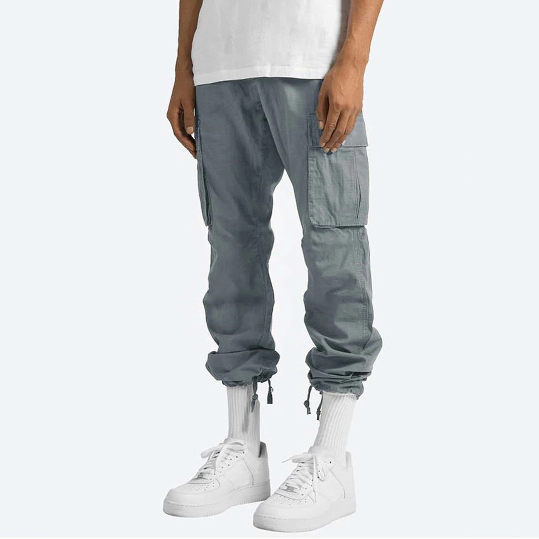 Pantaloni cargo grigi da uomo, tasche laterali, vestibilità comoda, abbinati a scarpe da ginnastica bianche e calze alte. Moda casual maschile.