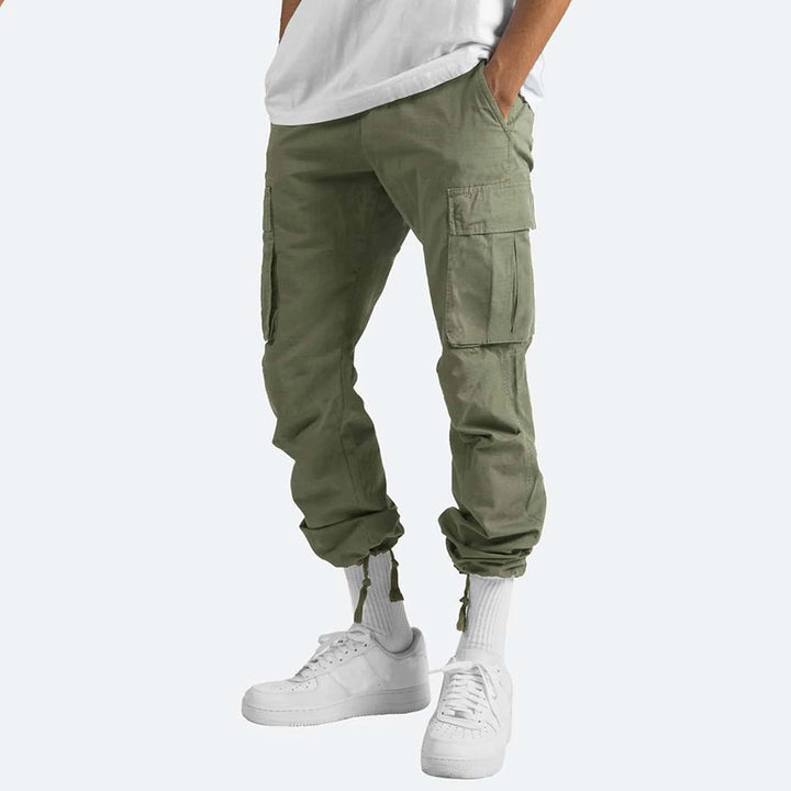 Pantaloni cargo verde oliva da uomo, tasche multiple, stile casual, abbinati a scarpe bianche e calzini alti. Ideali per look urbano e confortevole.