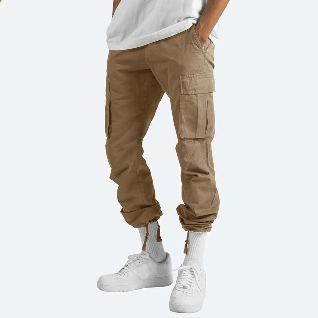 Pantaloni cargo beige da uomo, tasche laterali, vestibilità comoda, abbinati a scarpe bianche e calzini alti. Moda casual maschile.