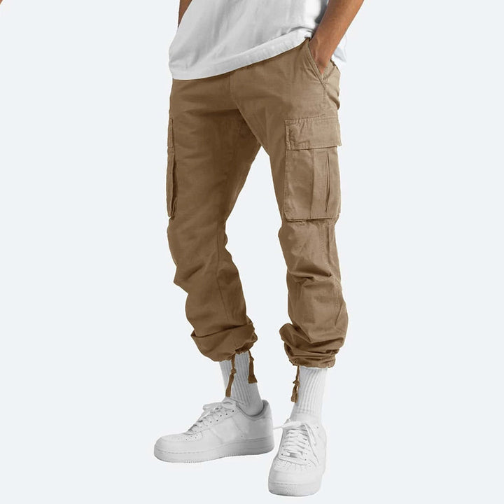 Pantaloni cargo beige da uomo, tasche laterali, vestibilità comoda, abbinati a scarpe bianche e calzini alti. Moda casual maschile.