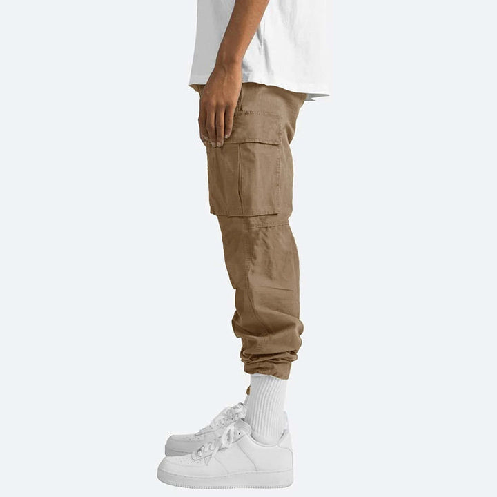 Pantaloni cargo uomo beige, tasche laterali, vestibilità comoda, stile casual, abbinati a scarpe sportive bianche, moda streetwear.
