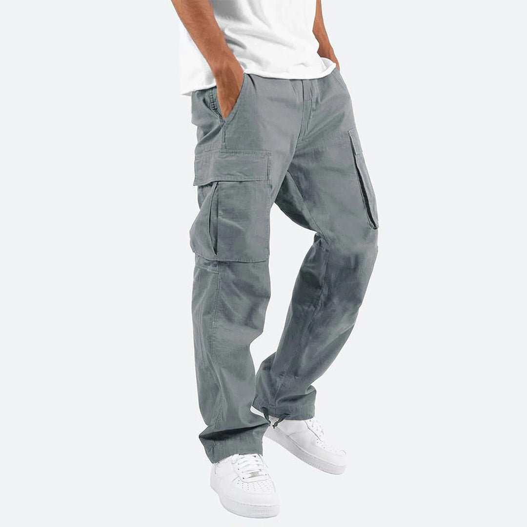 Pantaloni cargo grigi da uomo, tasche multiple, vestibilità comoda, abbinati a scarpe bianche e maglietta bianca. Stile casual moderno.