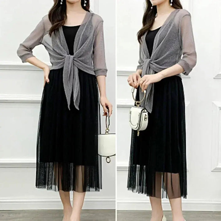 Abito lungo nero elegante con cardigan trasparente grigio, maniche a tre quarti, nodo frontale, perfetto per eventi formali e serate speciali.