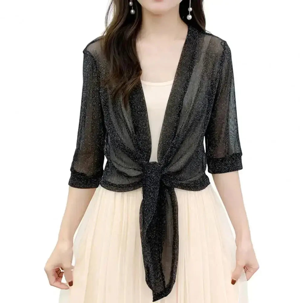 Blusa trasparente nera con maniche a tre quarti, nodo frontale, indossata su abito chiaro. Elegante coprispalle donna, moda serale.