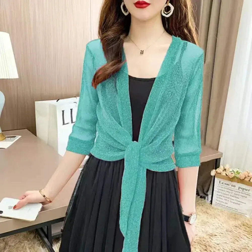 Donna con cardigan verde acqua su abito nero, orecchini a cerchio, collana e orologio. Moda elegante, abbigliamento femminile, stile casual chic.