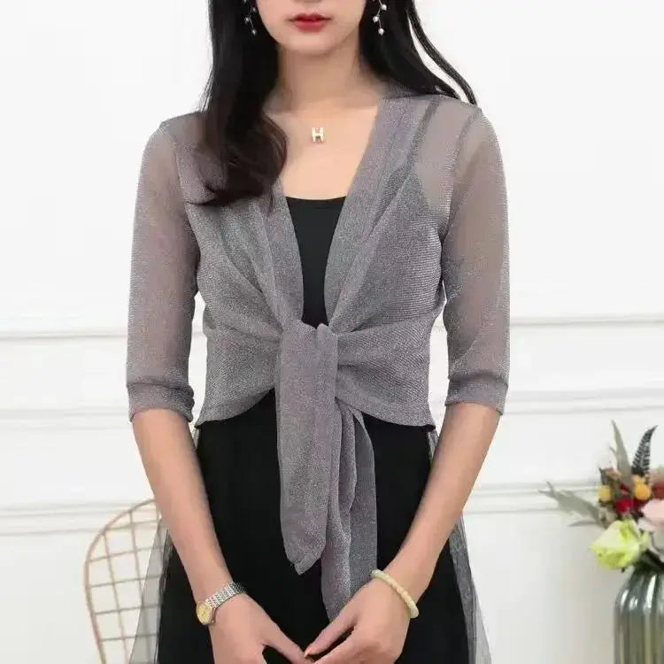 Donna con cardigan trasparente grigio, maniche a tre quarti, sopra abito nero elegante. Moda femminile, abbigliamento chic, stile moderno.
