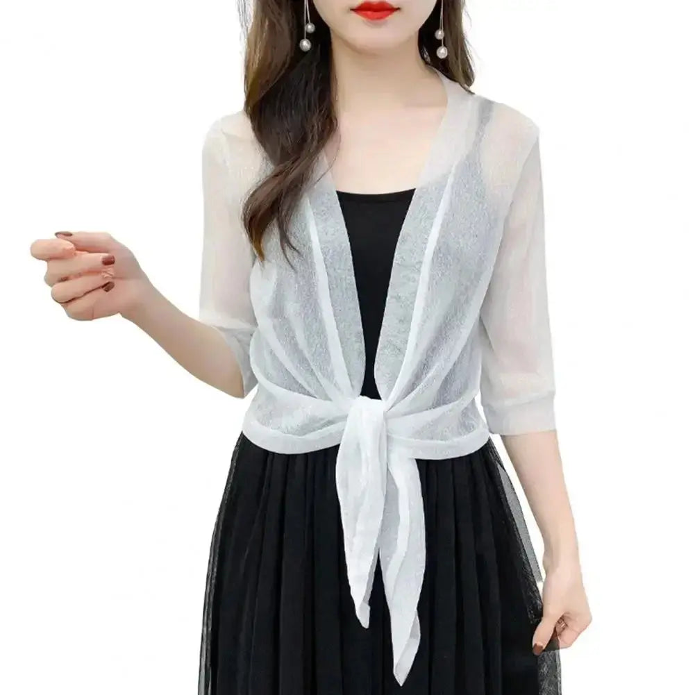 Donna con cardigan bianco trasparente annodato, sopra abito nero elegante. Moda femminile, abbigliamento estivo, stile casual chic.