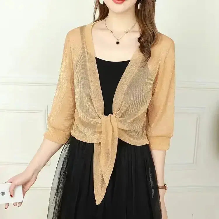Donna con cardigan beige trasparente annodato, sopra abito nero elegante. Moda femminile, abbigliamento estivo, stile casual chic.
