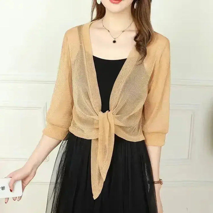 Donna con cardigan beige trasparente annodato, sopra abito nero elegante. Moda femminile, abbigliamento estivo, stile casual chic.