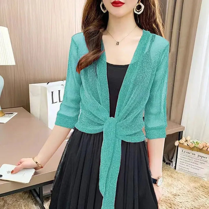 Donna con cardigan verde acqua su abito nero, in un ambiente moderno. Moda femminile elegante, abbigliamento casual chic, accessori minimal.