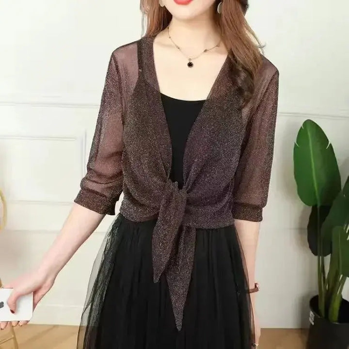 Donna con cardigan trasparente glitterato nero, abito nero elegante, pianta decorativa sullo sfondo. Moda femminile, abbigliamento da sera.