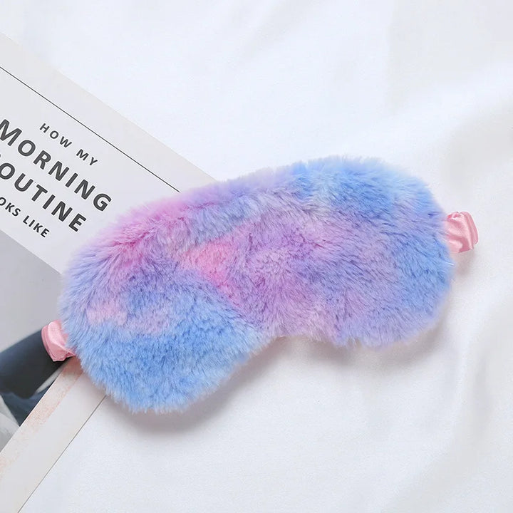 Maschera per dormire in peluche multicolore, sfumature blu e rosa, su lenzuolo bianco. Accessorio per il sonno, morbido e confortevole.