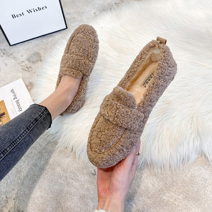 Scarpe mocassini in pelliccia sintetica marrone, comode e calde, su tappeto bianco. Ideali per l'inverno, moda donna, stile casual.
