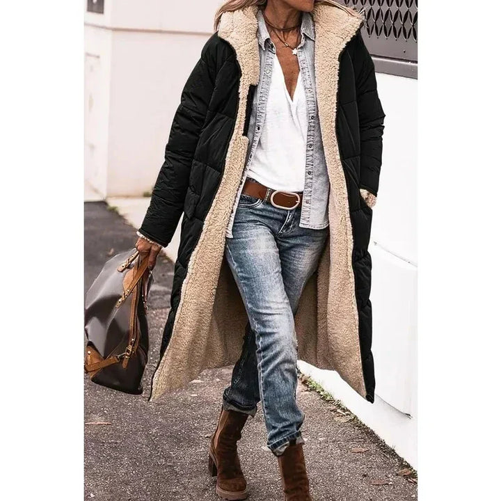 Cappotto lungo nero con interno in pelliccia sintetica beige, indossato con jeans e stivali marroni. Moda invernale donna, stile casual chic.