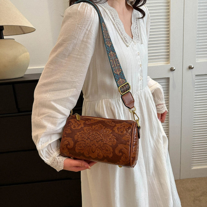Donna con abito bianco indossa borsa a tracolla in pelle marrone con motivo floreale. Accessorio moda elegante, perfetto per look casual chic.