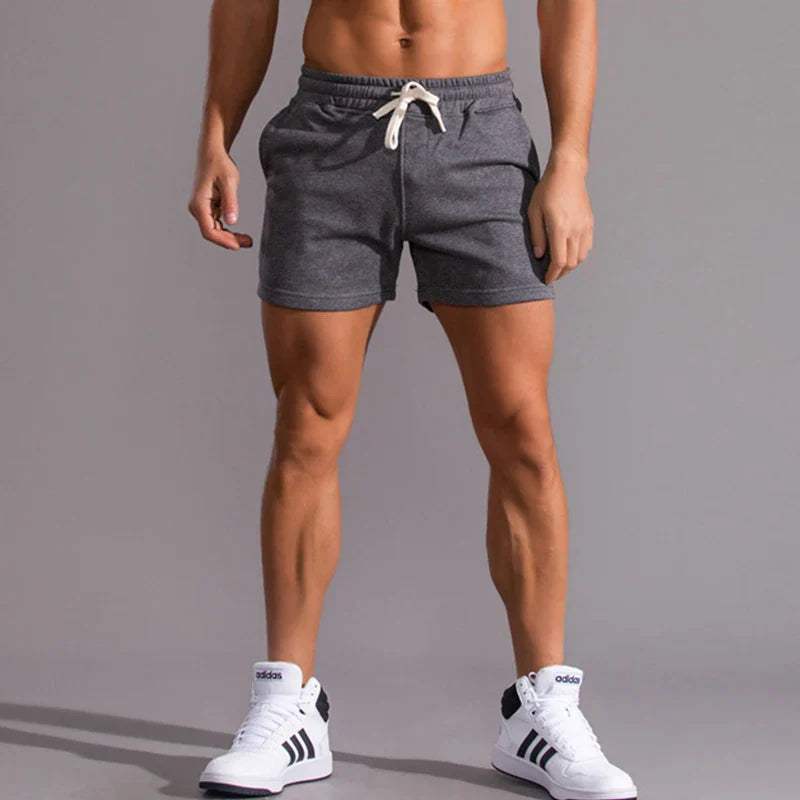 Shorts sportivi grigi da uomo, con coulisse bianca, indossati con scarpe da ginnastica bianche e nere. Abbigliamento casual estivo.