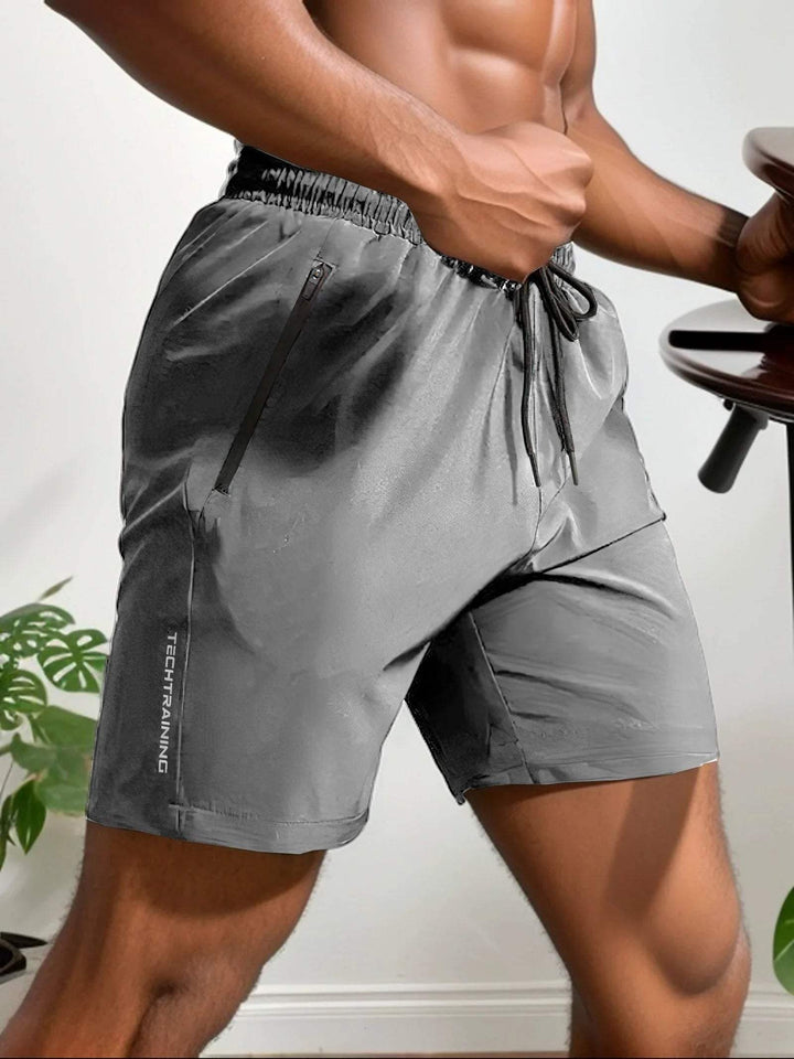 Shorts sportivi grigi da uomo, tessuto leggero, con tasche con zip e coulisse. Ideali per allenamento, palestra, fitness. Design moderno e funzionale.