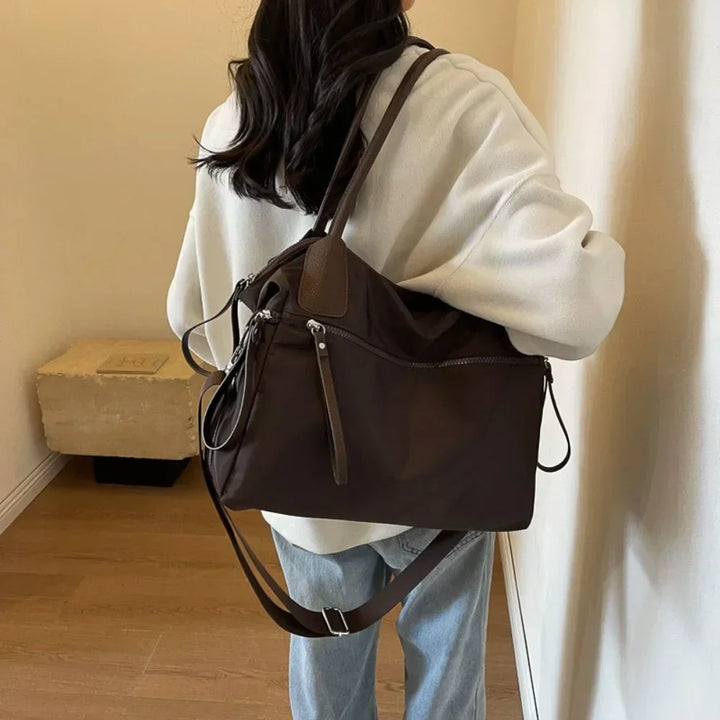 Donna con borsa a tracolla marrone, giacca bianca e jeans. Accessorio moda casual, ideale per shopping e viaggi. Stile urbano elegante.