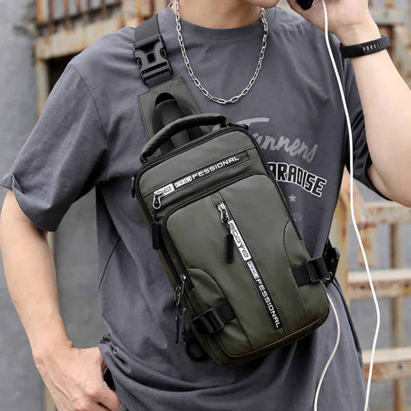 Uomo con borsa a tracolla verde militare, tasche multiple, cerniere nere, indossa maglietta grigia e catena argento, ascolta musica con auricolari.