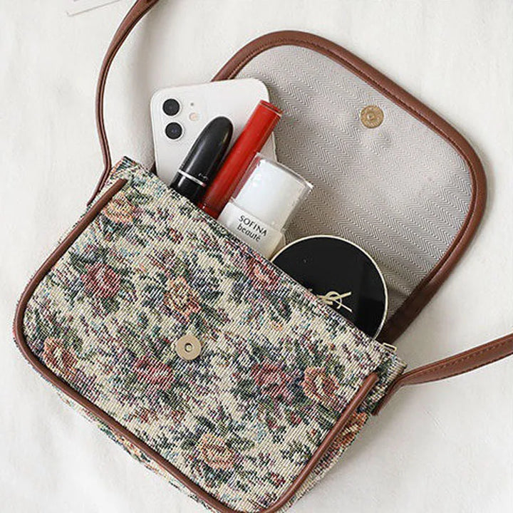 Borsa a tracolla floreale aperta con smartphone, rossetto, cipria e crema. Accessori moda donna, stile vintage, eleganza quotidiana.