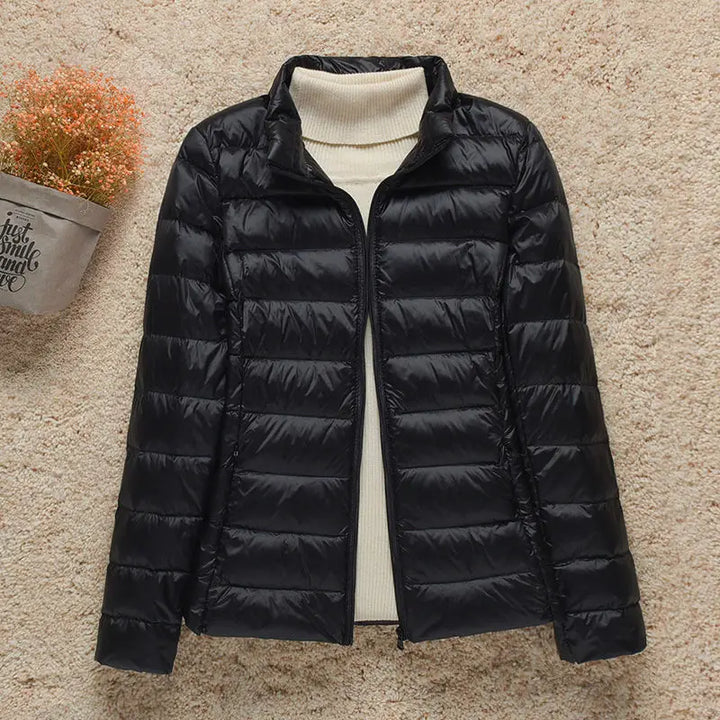Giacca invernale nera imbottita da donna su sfondo beige, con collo alto e chiusura a zip. Elegante e calda, ideale per la stagione fredda.