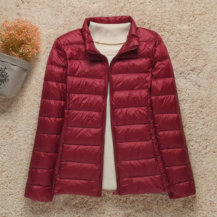 Giacca invernale trapuntata rossa da donna su sfondo beige, con collo alto e design elegante. Perfetta per moda autunno-inverno.