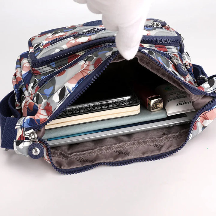 Borsa a tracolla floreale aperta, mostra tasche multiple con notebook, penne e accessori. Design colorato, ideale per organizzazione e stile.
