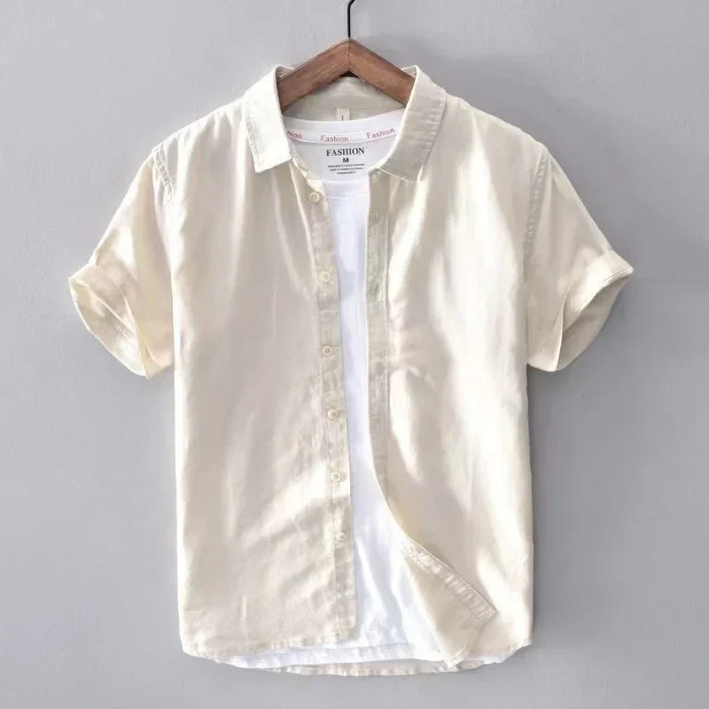 Camicia beige a maniche corte in cotone, appesa su gruccia di legno, sfondo grigio. Moda casual estiva, abbigliamento uomo elegante.