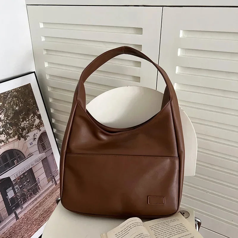 Borsa a spalla in pelle marrone su sedia bianca, design elegante e moderno, perfetta per moda donna. Accessorio versatile per ogni occasione.