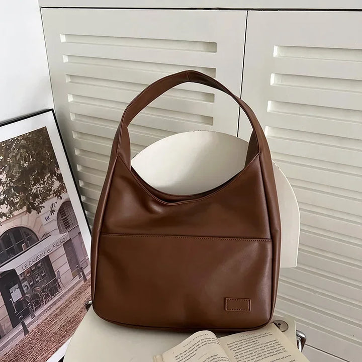 Borsa a spalla in pelle marrone su sedia bianca, design elegante e moderno, perfetta per moda donna. Accessorio versatile per ogni occasione.