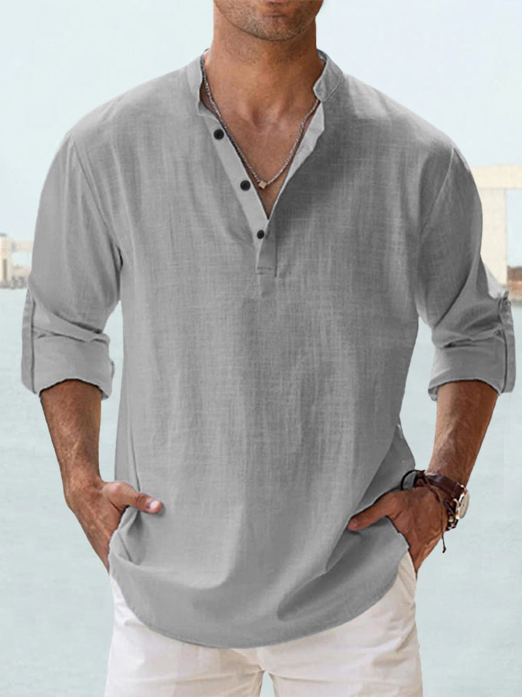 Camicia uomo lino grigia con colletto alla coreana, maniche lunghe arrotolate, abbinata a pantaloni bianchi. Stile casual estivo elegante.