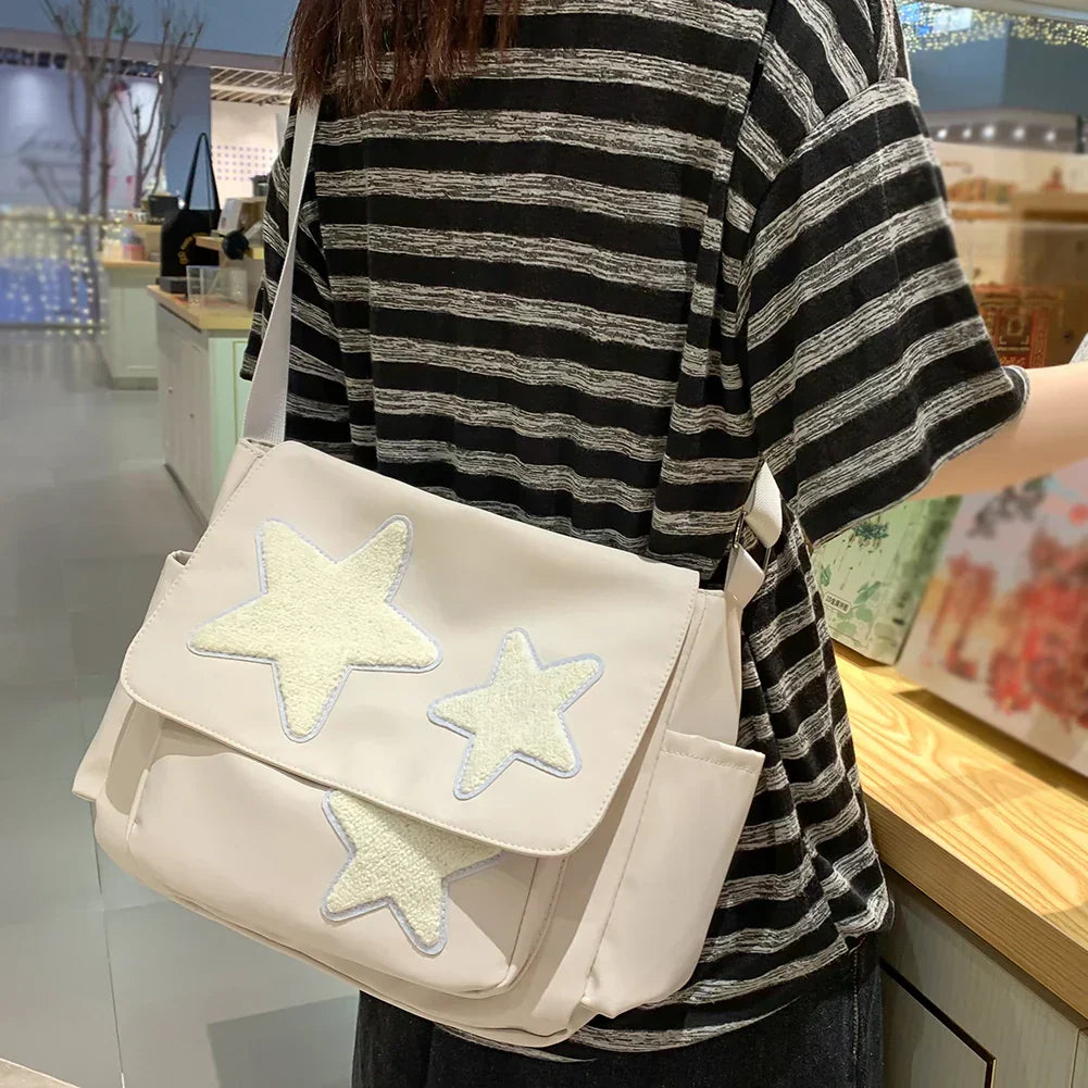 Borsa a tracolla bianca con stelle ricamate, indossata da una persona in maglietta a righe. Accessorio moda casual, ideale per shopping e uscite.