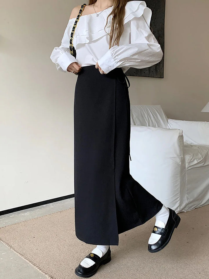 Blusa bianca monospalla con volant, abbinata a gonna lunga nera e mocassini neri con calzini bianchi. Look elegante e moderno per donna.