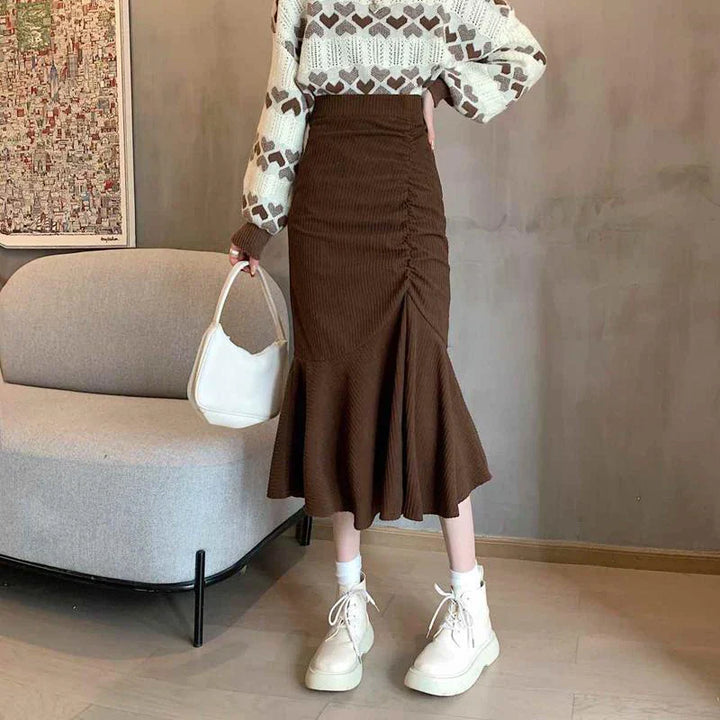 Donna con maglione a cuori e gonna marrone a pieghe, borsa bianca e stivali alti. Moda autunnale, abbigliamento casual chic.