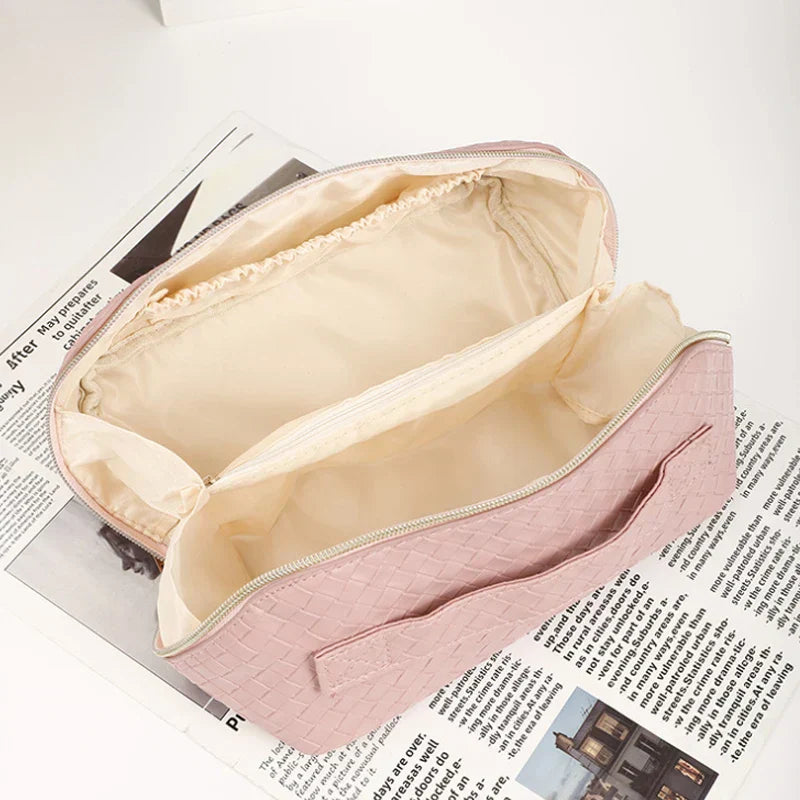 Borsa cosmetica rosa intrecciata aperta su giornale, design elegante, scomparti spaziosi, ideale per trucco e accessori da viaggio.