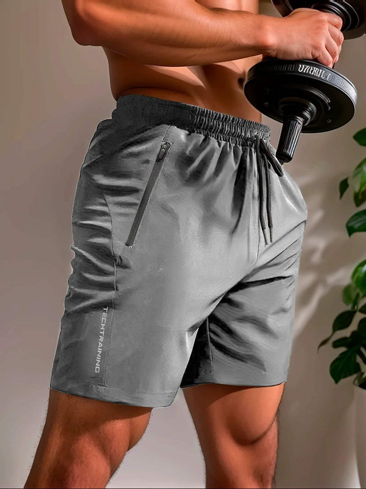 Pantaloncini sportivi grigi da uomo, con tasca con zip, indossati durante l'allenamento con manubri. Abbigliamento fitness traspirante e comodo.