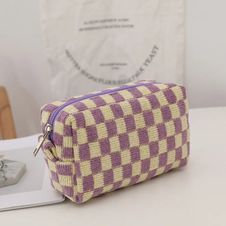 Astuccio a scacchi viola e giallo, tessuto in maglia, con cerniera argentata, su tavolo bianco. Design moderno, accessorio moda pratico.