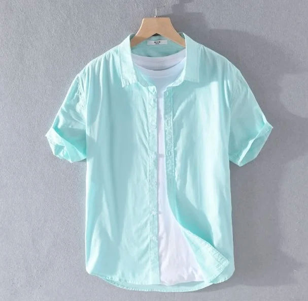 Camicia azzurra da uomo in cotone, maniche corte, su gruccia, sfondo grigio. Ideale per moda estiva casual.