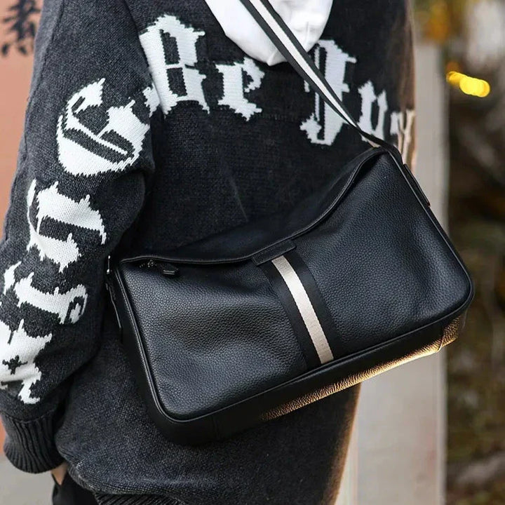 Borsa a tracolla in pelle nera con striscia centrale grigia, indossata su felpa con cappuccio. Accessorio moda uomo, stile casual ed elegante.