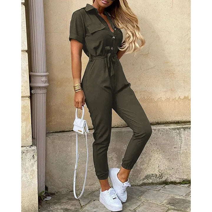 Donna in tuta verde oliva con cintura, scarpe da ginnastica bianche e borsa a tracolla bianca. Look casual chic, moda femminile urbana.