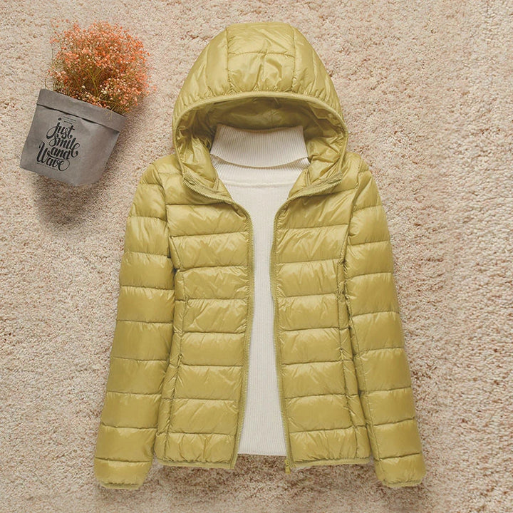 Giacca invernale donna gialla con cappuccio, imbottita, su sfondo beige. Moda autunno-inverno, abbigliamento caldo e casual.