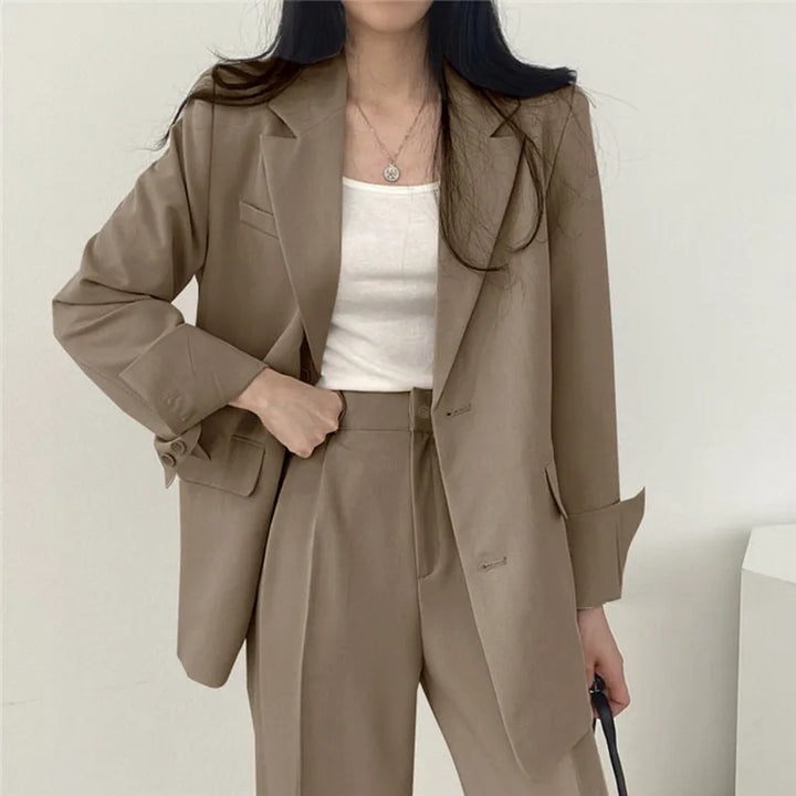 Donna in abito elegante beige, giacca e pantaloni coordinati, indossa top bianco. Moda femminile, abbigliamento formale, stile business casual.