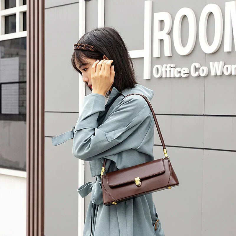 Donna con cappotto azzurro indossa borsa a tracolla marrone in pelle, design elegante e moderno, perfetta per ufficio e uso quotidiano.
